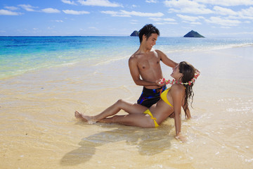 man gives a flower lei to a woman on the beach in hawaii
