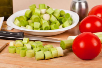 Fresh chopped leeks on a wooden board with red tomatoes