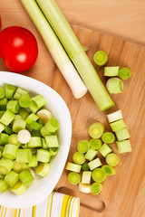 Fresh chopped leeks on a wooden board with red tomatoes