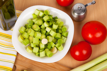 Fresh chopped leeks on a wooden board with red tomatoes