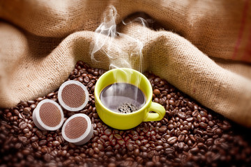 Steaming coffee cup with beans, capsule  and hessian sack