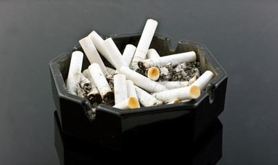 black ashtray with cigaretes on black table