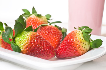 erdbeeren auf Teller, milchshake im Hintergrund