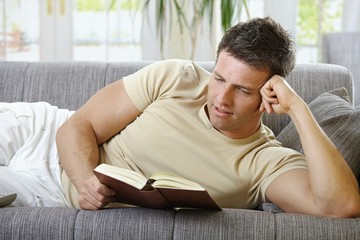 Smiling man lying on sofa reading