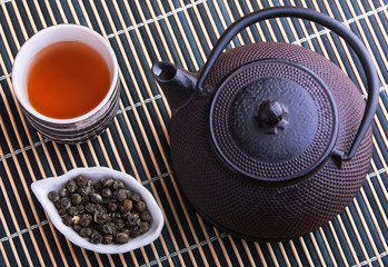 Cast iron TeaPot with teacup and tea leaves on a bamboo mat