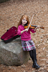 Beautiful little girl with long red hair outdoors with violin