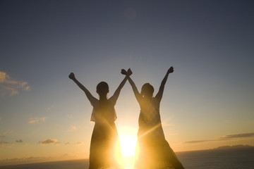 夕暮れに両手を空に広げる女性2人のシルエット