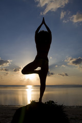 A silhouette of a woman facing the sunset in a yoga pose