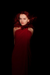 Fototapeta premium glamour portrait redhaired woman in a red dress on black backgro