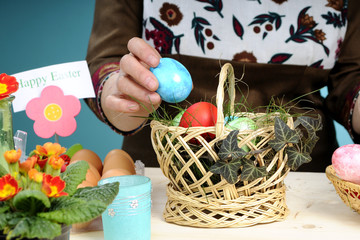 human hand decorating easter basket with eggs and plants