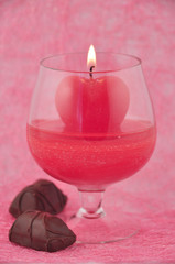 Candle-heart in goblet on red background with sweetmeat