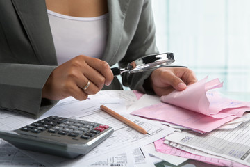 Businesswoman checking bills using magnifying glass