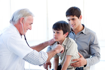 Obraz premium Senior doctor examining a little boy with his father