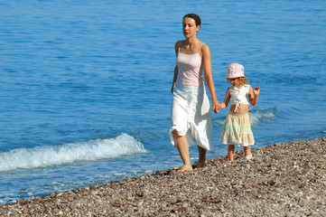 Woman with small girl go on seaside