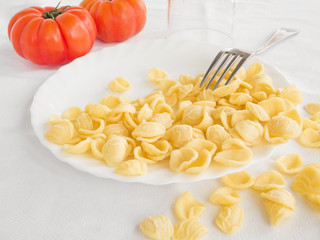 Orecchiette on white dish with fork and tomatoes.