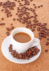Small white cup of coffee with coffee grain on brown background