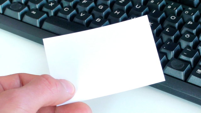 hand with white card in front of a computer keyboard