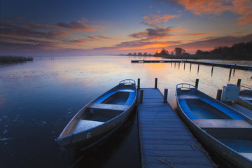 Peaceful sunrise with dramatic sky and boats and a jetty - 21172226