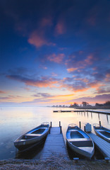 Peaceful sunrise with dramatic sky and boats and a jetty - 21172284