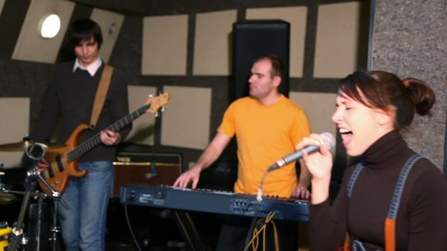 girl with microphone singing in studio, musicians against