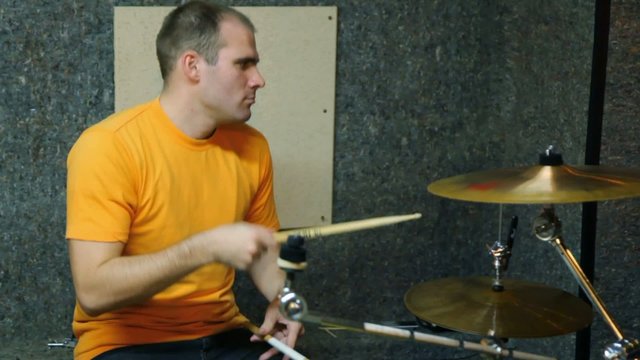 yellow T-shirted drummer playing on drums in recording studio