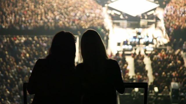silhouettes of two dancing women against concert hall