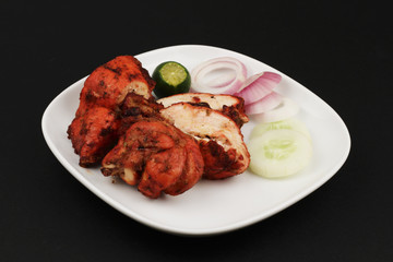Tandoori chicken with some garnishing on a black background