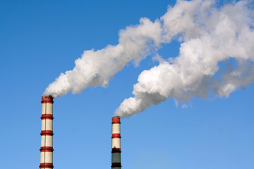 Two huge steaming plant power plant tubes over blue sky