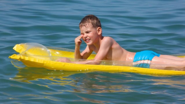 smiling young boy oaring on inflatable mattress in sea