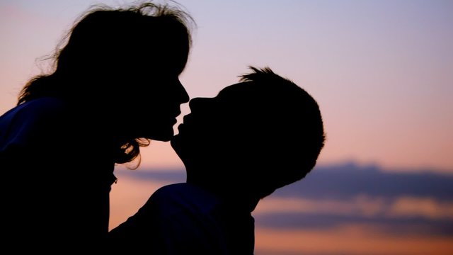 silhouettes of man and woman kissing, sunset sky in background