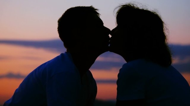 silhouettes of man and woman kissing, sunset sky