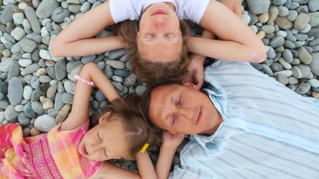 happy family of three persons lying on pebble beach, top view