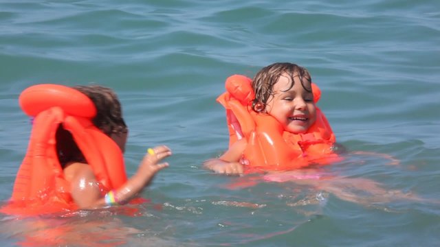 two little girls dressed in life jackets swimming in water