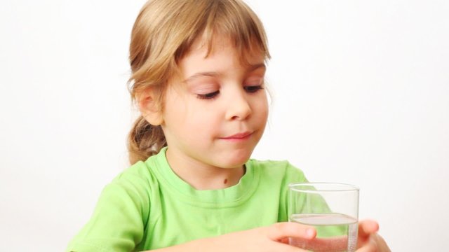 small girl drinks water from glass and smiles on white