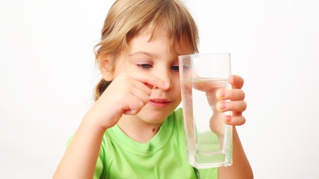 girl shows by little on glass of water and smiles on white