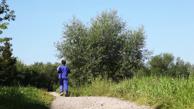 man in turn blue gym suits runs back on lane in park in summer