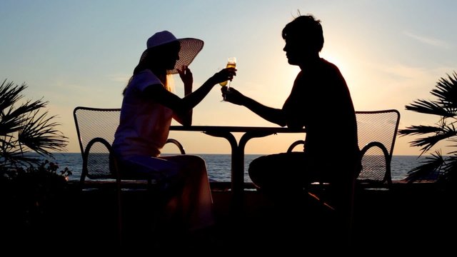 silhouettes of couple drink brotherhood sits at table, sunset