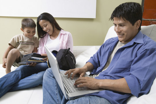 father using laptop and mother and son looking at dvds on couch