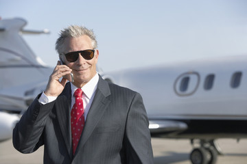 businessman standing on landing strip near private jet talking on mobile