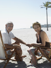 senior couple on sunloungers on tropical beach