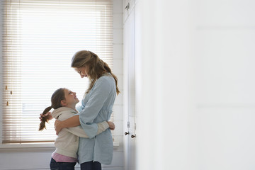 mother and daughter embracing standing in front of window
