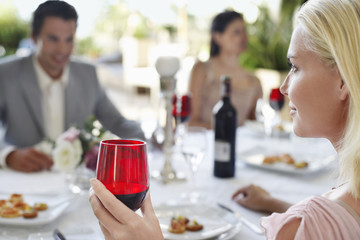 young woman holding wineglass sitting at table with friends