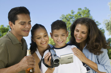 boy (13-15) looking into camcorder with family outdoors.