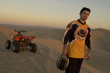 man standing by quad bike in desert at sunset