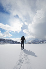 man walking in snowshoes through snow back view