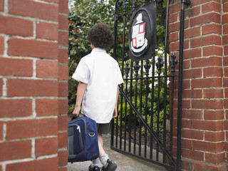 elementary schoolboy walking through school gate back view