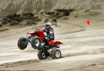 Teen riding ATV in sand dunes doing a wheelie