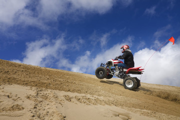 Male riding ATV up sand dune hill