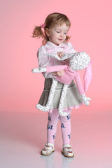 Little girl is playing with rabbit toy in studio on pink