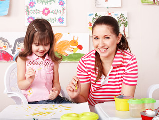 Child with teacher draw paints in play room.